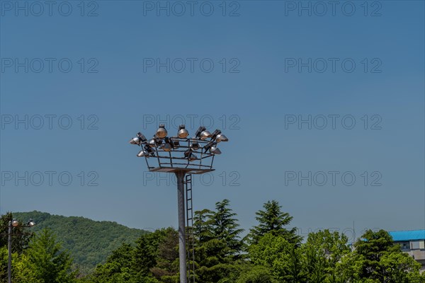 Floodlight tower over trees under a bright daytime sky, in South Korea