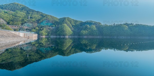 Still morning at a dam with forested hills and perfect reflections in the reservoir, in South Korea