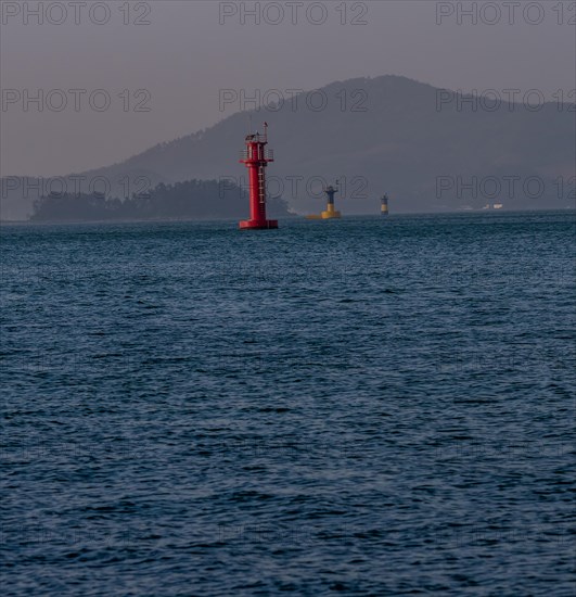 Three small lighthouses in a harbor with small mountains shrouded in fog and mist in the background in Namhae South Korea