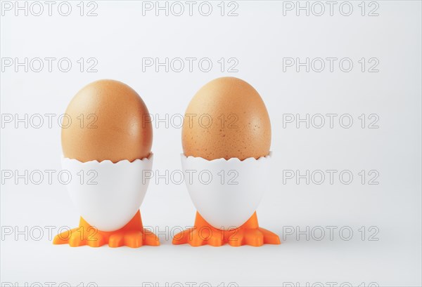 Two fresh eggs in an egg cup in the shape of a chicken on a white background