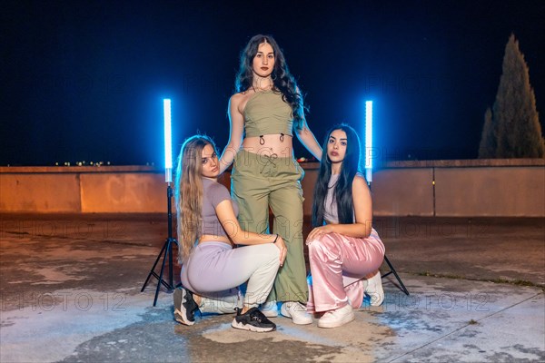 Trap music dancers posing together in a night set with blue neon lights in a urban park