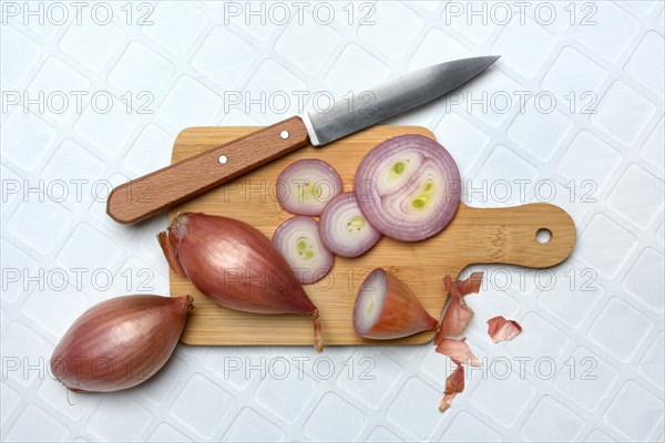 Shallots on wooden board with knife, Allium cepa