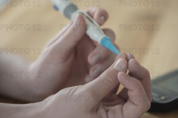 On the left a child's hand holding a lancet, lancing device, and pricking itself to determine the blood glucose level, wooden table as background, measuring device device blurred on the right, blood glucose measurement, diabetes treatment, glucose measurement, Ruhr area, Germany, Europe