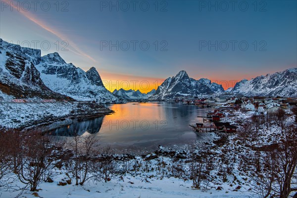 Sunset casting warm hues over a tranquil fjord surrounded by snow-covered mountains, Lofoten