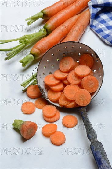 Carrot slices in colander and wooden spoon, Daucus carota