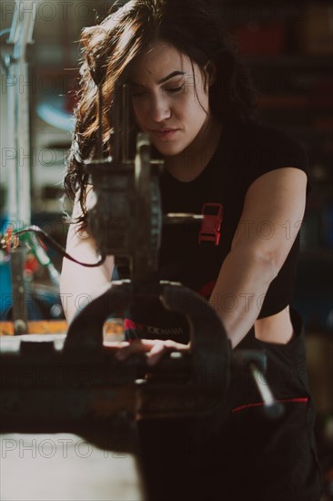 Close-up of a hispanic female mechanic at work, exerting effort on a mechanical piece with expertise in a workshop, a complete tool panel in background with bokeh effect, traditional male jobs by Mixed-race latino woman