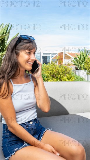 A woman is sitting on a couch and talking on her cell phone. She is smiling and she is enjoying her conversation