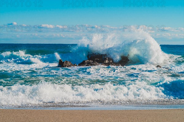 Waves full of foam crash with energy onto a rocky shore under clear weather, in South Korea