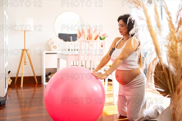 Horizontal photo of a beauty pregnant woman doing exercises with Pilates ball at home