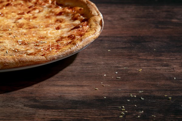 Freshly baked pizza with cheese and oregano on a dark wooden table