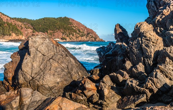 Foamy waves hitting the rocky shores of a vibrant blue sea on a sunny day with a clear sky, in South Korea