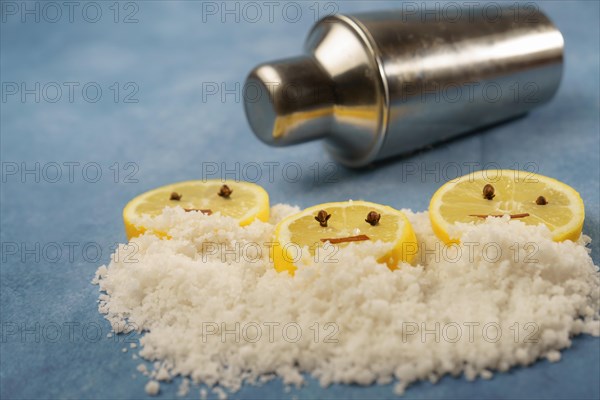 Lemon slices with cloves and cinnamon forming a smiley face on a pile of salt next to a shaker with blue background with copy space