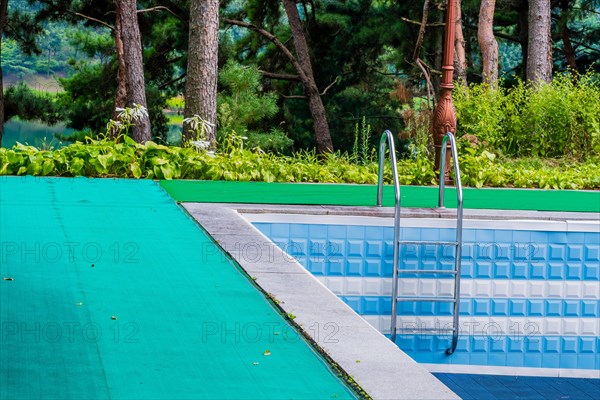 Outdoor swimming pool with a ladder, surrounded by a green mat and blue tiles, in South Korea