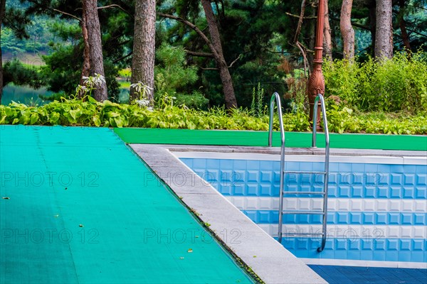 Outdoor swimming pool with a ladder, surrounded by a green mat and blue tiles, in South Korea