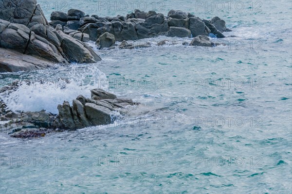 Waves crash onto boulders on the shore under a blanket of clouds, in South Korea