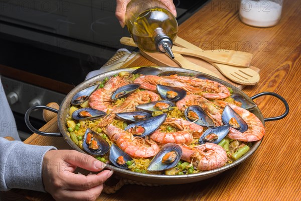 Pouring olive oil into a seafood paella, enhancing the flavors of this classic Spanish dish, typical Spanish cuisine, Majorca, Balearic Islands, Spain, Europe