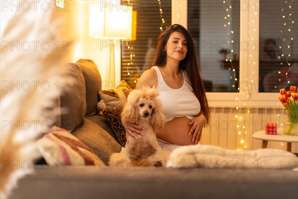 Portrait of a pregnant woman and dog sitting together on the sofa at home at night