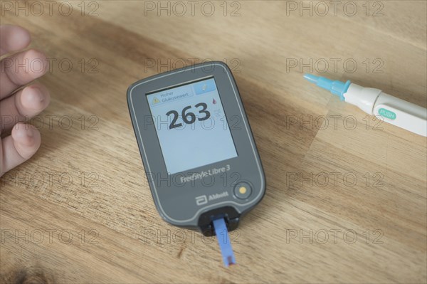 Blood glucose meter with test strips and a drop of blood lies in the centre of a wooden table, high value, on the left the fingers of a child, on the right the lancing device, lancet, blood glucose measurement, diabetes treatment, glucose measurement, Ruhr area, Germany, Europe