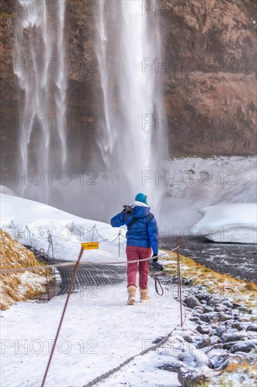 Photographer woman in winter in Iceland visiting Seljalandsfoss waterfall