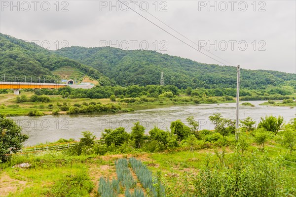 Overcast view of a river landscape with a train bridge in the distance and green mountains, in South Korea