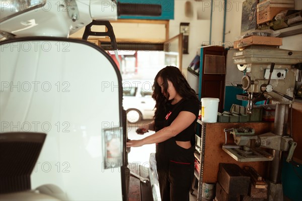 Mechanic standing by a classic scooter in a sunlit workshop full of tools, latino female in traditional masculine jobs concept, feminine power in real life