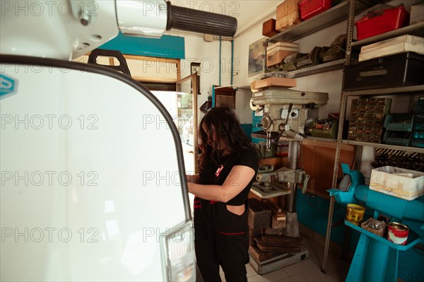 Focused hispanic young sensual long haired brunette woman mechanic inspecting a vintage scooter in a well-utilized workshop, latino female in traditional masculine jobs concept, feminine power in real life