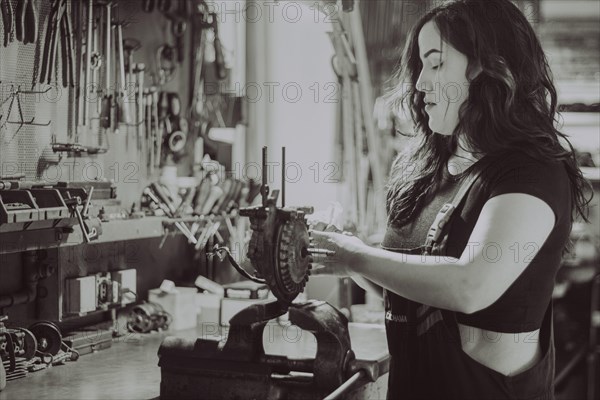 Woman concentrating on mechanical work at a workshop bench, real women performing traditional man jobs of the past, black and white photograph
