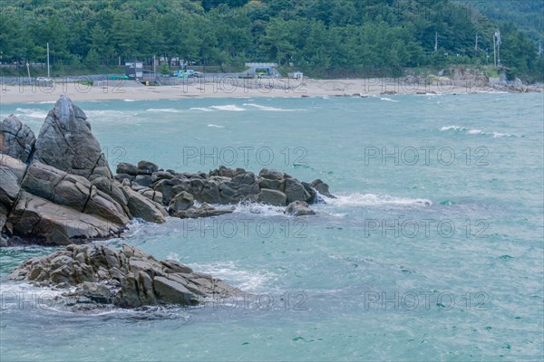 A view of a rocky coast with a sandy beach in the distance under an overcast sky, in South Korea