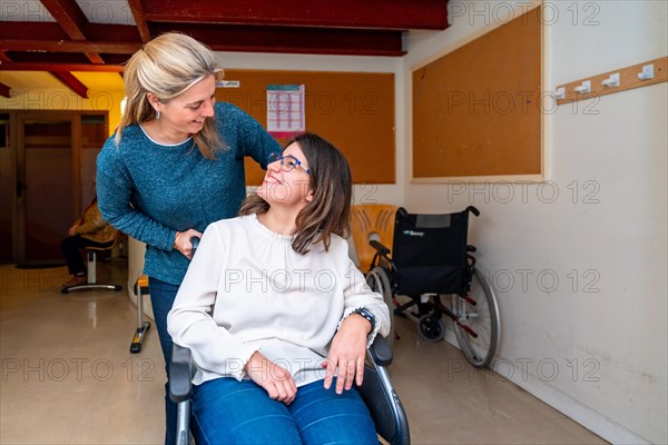 Caregiver pushing the wheelchair of a disabled woman in a day center for people with special needs