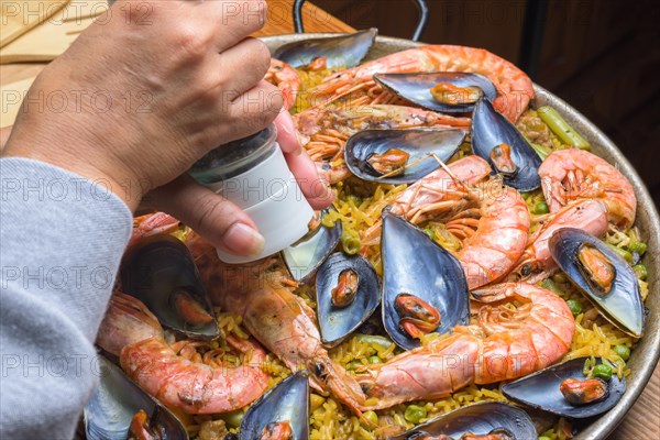 Close-up of a hand seasoning traditional seafood paella with rich colors, typical Spanish cuisine, Majorca, Balearic Islands, Spain, Europe