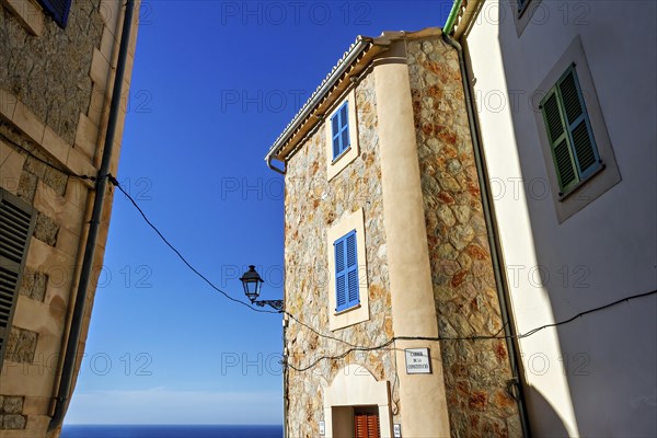 A picturesque stone building with blue shutters beside a cobblestone street under a blue sky, Hiking tour from Estellences to Banyalbufar, Mallorca