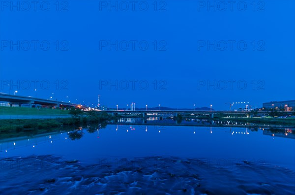 Blue hour scene of highway bridges reflected in calm water with city lights, in South Korea