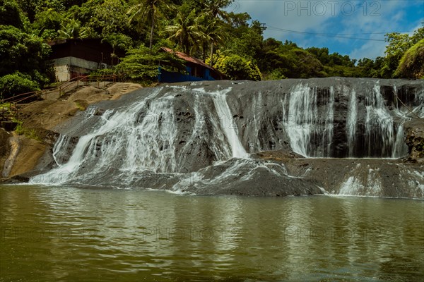 Landscape of a waterfall taken with ND filter with trees and blue sky in the background and water basin in the foreground in Guam