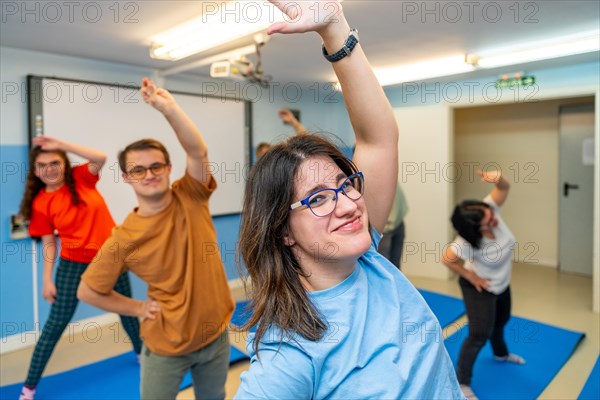 Happy people with special needs exercising in a gym smiling and looking at camera standing stretching the back