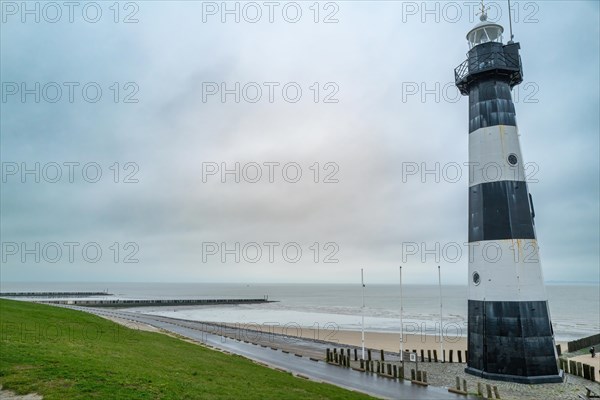 A black and white lighthouse with beach piles and a green area on a cloudy day, Breskens, Zeeland, Netherlands
