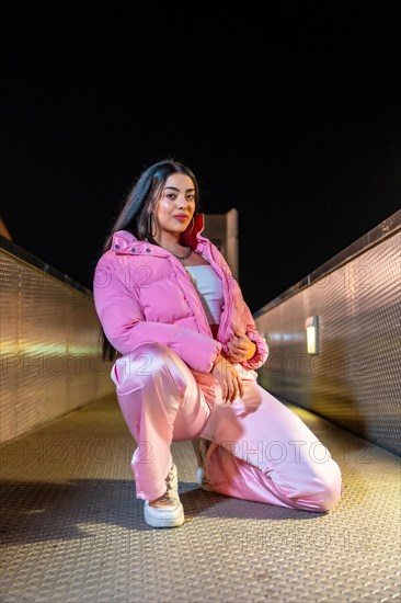 Vertical portrait of a female beauty and young hip hop dancer in pink clothes kneeling outdoors at night