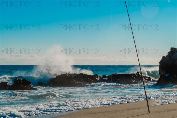 A dramatic maritime scene with a fishing rod overlooking waves crashing onto rocky shores, in South Korea