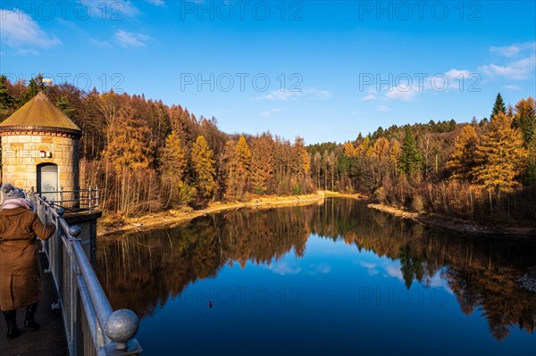 People walking along a dam, surrounded by colourful autumn trees under a blue sky, Ronsdorfer Talsperre, Ronsdorf, Wuppertal, Bergisches Land, North Rhine-Westphalia