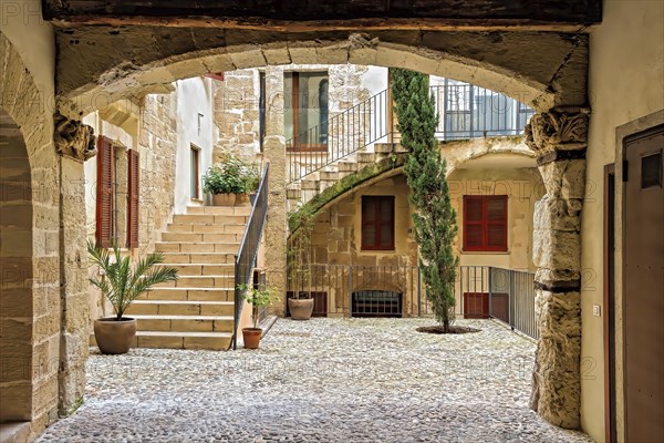 A serene cobblestone courtyard with potted plants and an archway leading to stairs, Palma De Mallorca