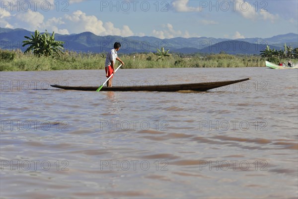 A child stands on a narrow boat on a quiet river, Inle Lake, Myanmar, Asia