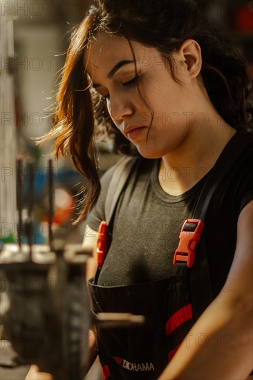 Woman mechanic in deep focus and contemplation while making mechanical adjustments in dimly lit solitude, a complete tool panel in background with bokeh effect, traditional male jobs by Mixed-race latino woman