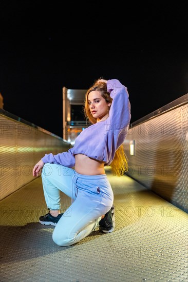 Vertical portrait of a caucasian blonde and sensual young woman with urban hip hop style outdoors at night