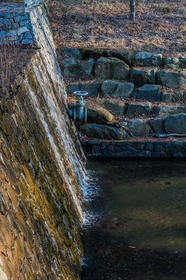 Water flows from a pipe in a stone wall during twilight creating a small cascade, in South Korea