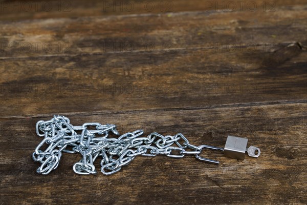 Shiny chain with open padlock with key on a wooden table in a park