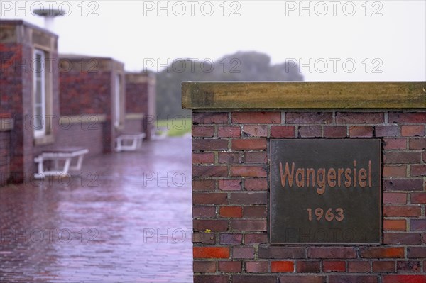 Wangersiel 193, metal sign at the harbour of Horumersiel on a red brick wall, in the background benches and the paved path to the dike, Horumersiel, Wangerland, North Sea coast, Germany, Europe