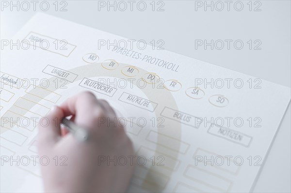 Diabetes log, daily log of food and insulin administration, food log, hand of a child holding a pen and appearing to fill in the log, the paper lies on a white table, Ruhr area, Germany, Europe