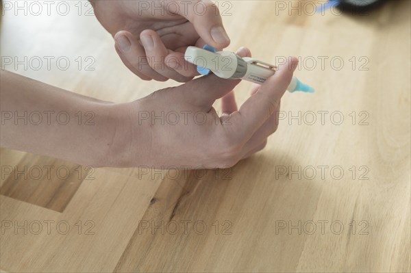 A lancet, lancing device, is held by a child in the right hand and drawn up to determine the blood sugar value, wooden table as background, measuring device device blurred in the background, blood sugar measurement, diabetes treatment, glucose measurement, Ruhr area, Germany, Europe