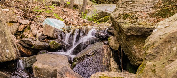 White plastic bag full of trash in stream of water cascading over large rocks and boulders in South Korea