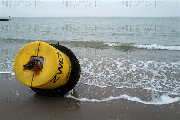 Yellow buoy on a sandy beach with waves in the background on a cloudy day, Westkapelle, Zeeland, Netherlands
