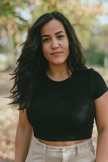 Close-up portrait of a smiling Cheerful hispanic young woman in a black shirt, with a selective soft-focus natural background, blurred background with bokeh, daytime, AI generated